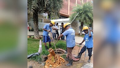 Workers in blue uniforms and yellow helmets repairing a manhole in Hyderabad.