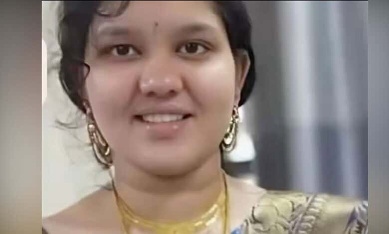 A woman smiling, wearing traditional Indian attire and jewelry, indoors.