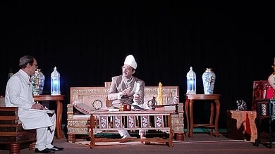 Historical scene with Salar Jung III in traditional attire on stage with two men, ornate vases, and stage.