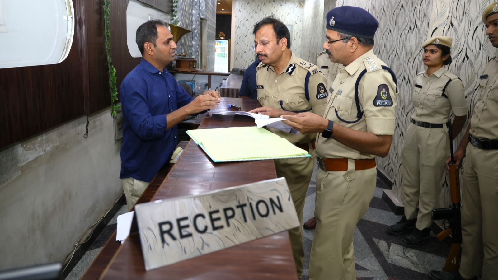Police officers engaging with a visitor at the reception desk in a government or institutional setting.
