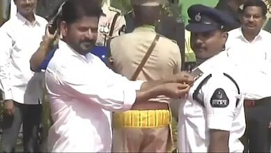 Man pinning badge on police officer during a public event, with onlookers and officials present in the ba.