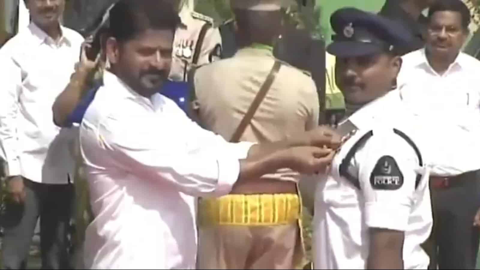 Man pinning badge on police officer during a public event, with onlookers and officials present in the ba.