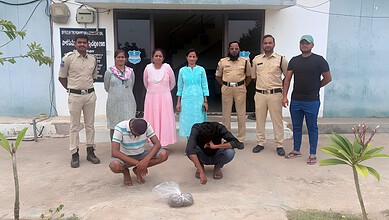 A woman and a man kneeling on the ground with a bag of items, surrounded by police officers and other ind.