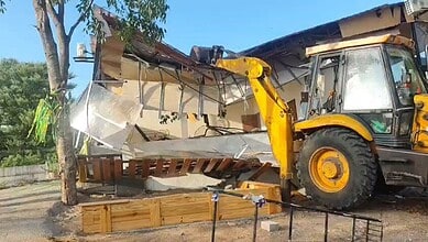 Excavator demolishing a building on a sunny day in Hyderabad.