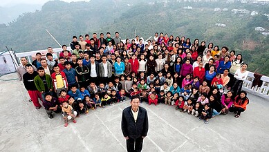 Group of diverse people gathered outdoors on a mountain terrace, posing for a photo.