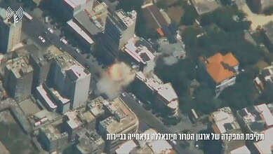 Aerial view of a building explosion in an urban area with smoke and debris.