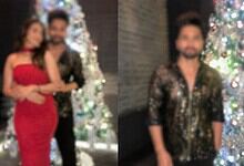 Bollywood actor in black and gold shirt with woman in red dress near Christmas trees.