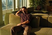 Jaaved Jaaferi sitting on a green sofa in a bright, modern living room with city views.