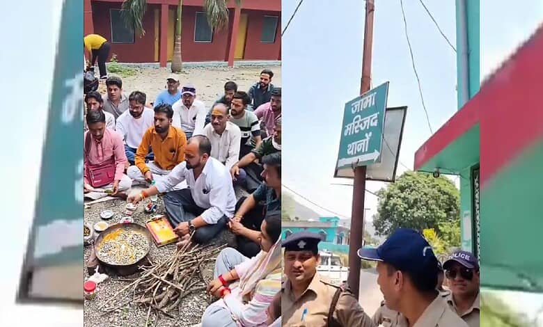 A group of people sitting on the ground around a traditional fire cooking setup outdoors, with police off.