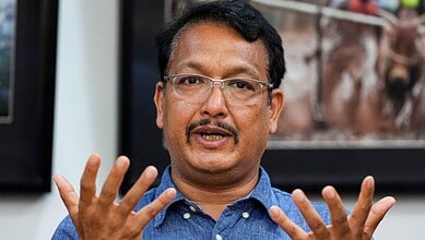 A man speaking passionately during a discussion or interview, wearing glasses and a blue shirt.