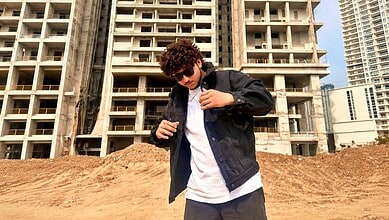Young man with curly hair wearing sunglasses and a black jacket at a construction site in Hyderabad.