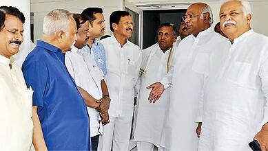 A group of Indian men engaged in a discussion indoors, dressed in traditional and formal attire, with a f.