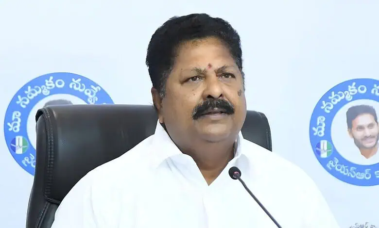 A woman in a white shirt speaking at a press conference with a microphone, seated in front of a blue logo.