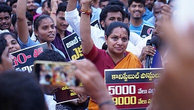 Kavitha speaking at a protest rally with supporters holding placards in Telangana.