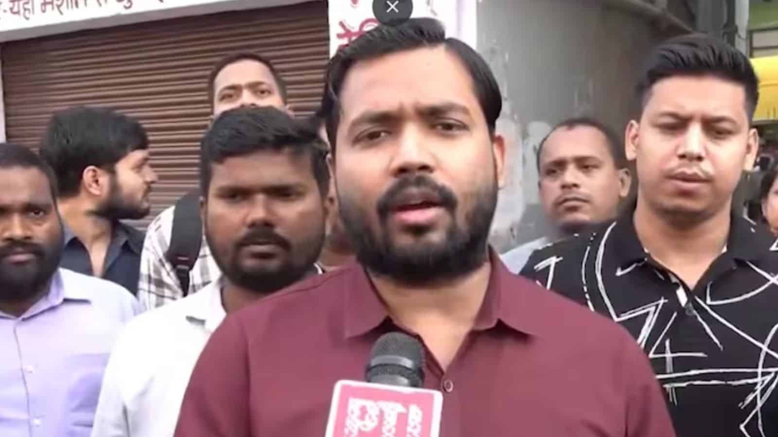 A man speaking into a microphone during a public event or protest with a group of people behind him.