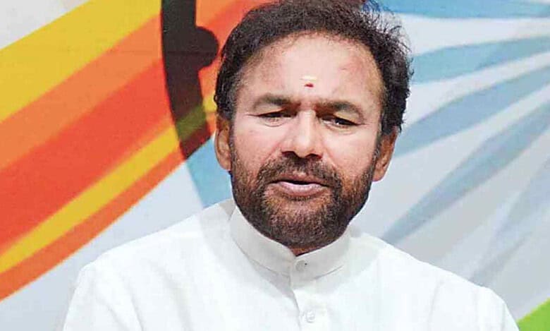 Kishan Reddy speaking at a press conference with Indian flag colors in background.