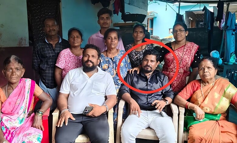 A woman in a black saree and a man in a white shirt sitting in the centre surrounded by a group of women.