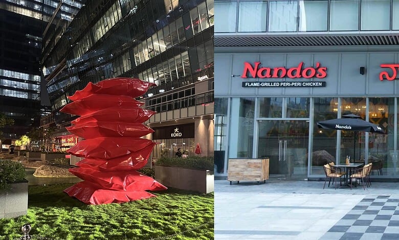 A vibrant red sculpture outside a modern building with Nando's restaurant signage.
