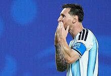 Lionel Messi in Argentina jersey, celebrating with hand over mouth, blue background.