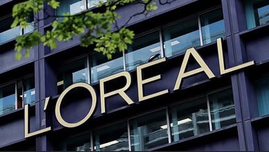 L'Oréal headquarters building with large logo on modern glass facade, reflecting urban surroundings.