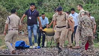 Police and officials carrying a bomb disposal device on railway tracks in a rural area.