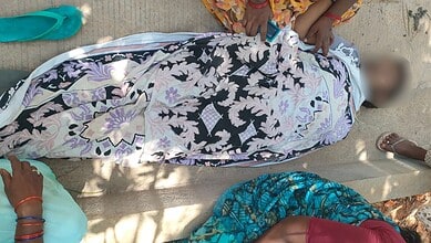 A person lying on the ground wrapped in a floral cloth with children nearby.