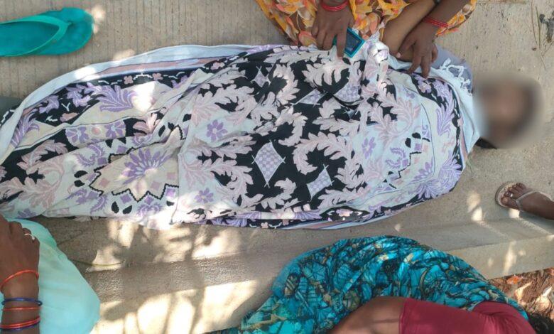 A person lying on the ground wrapped in a floral cloth with children nearby.