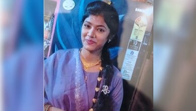 Young woman smiling in traditional purple saree with gold jewellery at a tech store in India.