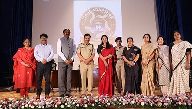 Empowered women and officials at the Naragadashak event on stage with a floral display in front.