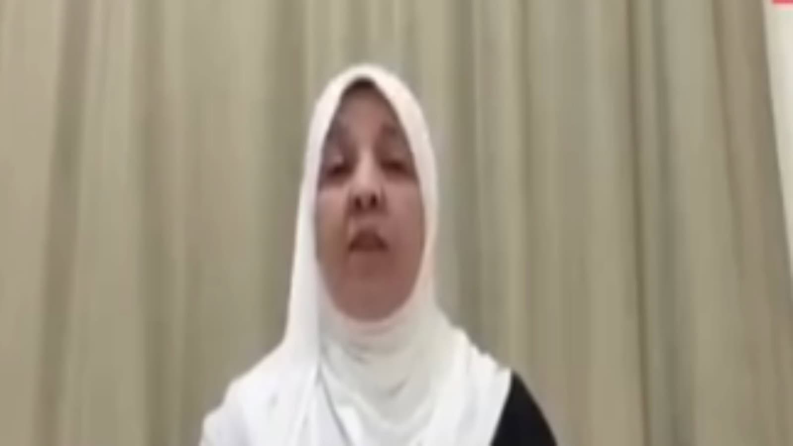 A woman wearing a white hijab and black attire speaking passionately during a public event.