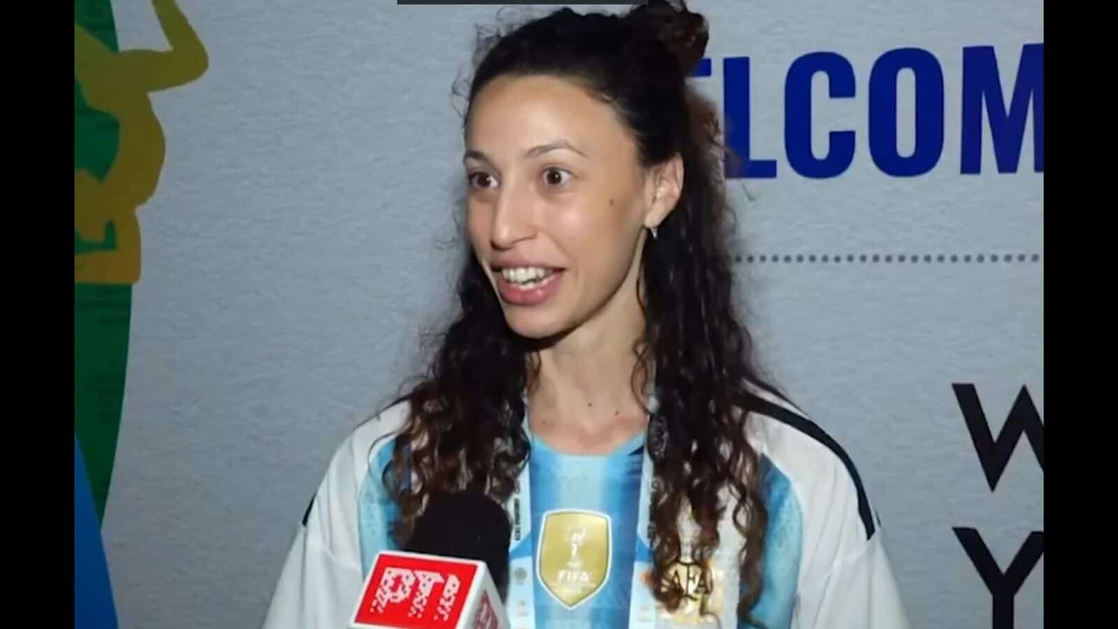 An image of Indian cricketer Smriti Mandhana speaking at a public event, wearing a sports jersey with a s.