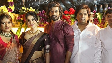 A group of five people dressed in traditional and formal attire at a cultural celebration, with vibrant f.
