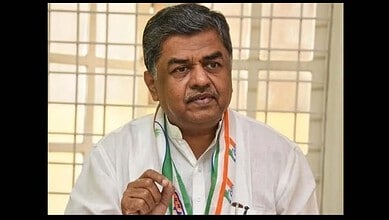 Indian politician speaking during an interview, wearing a white shirt and a tricolour scarf, in front of.