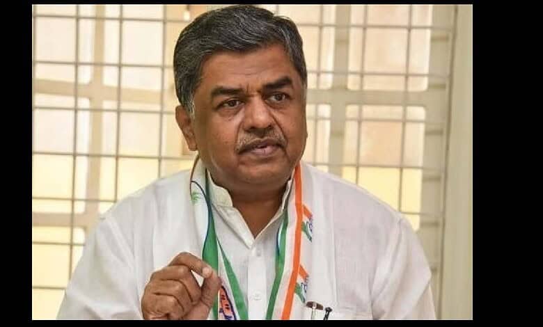 Indian politician speaking during an interview, wearing a white shirt and a tricolour scarf, in front of.
