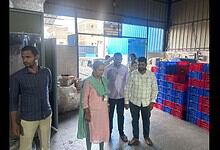 A woman and four men inspecting goods inside a warehouse with stacked plastic crates and large bags.