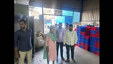 A woman and four men inspecting goods inside a warehouse with stacked plastic crates and large bags.