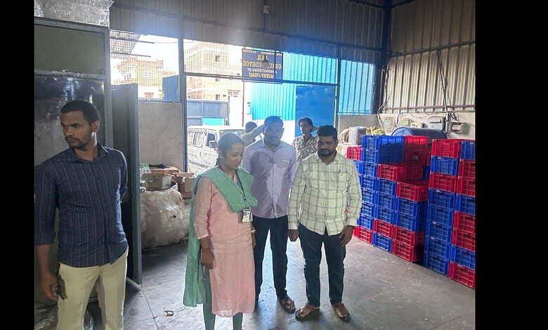 A woman and four men inspecting goods inside a warehouse with stacked plastic crates and large bags.