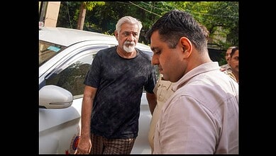 A man in a white shirt talking to an older man with a beard and black t-shirt outdoors.