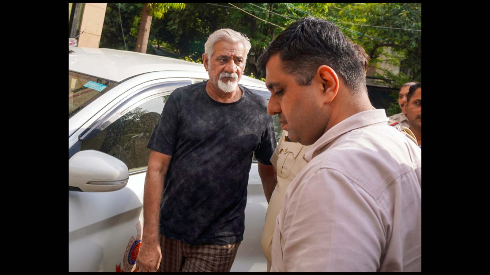 A man in a white shirt talking to an older man with a beard and black t-shirt outdoors.