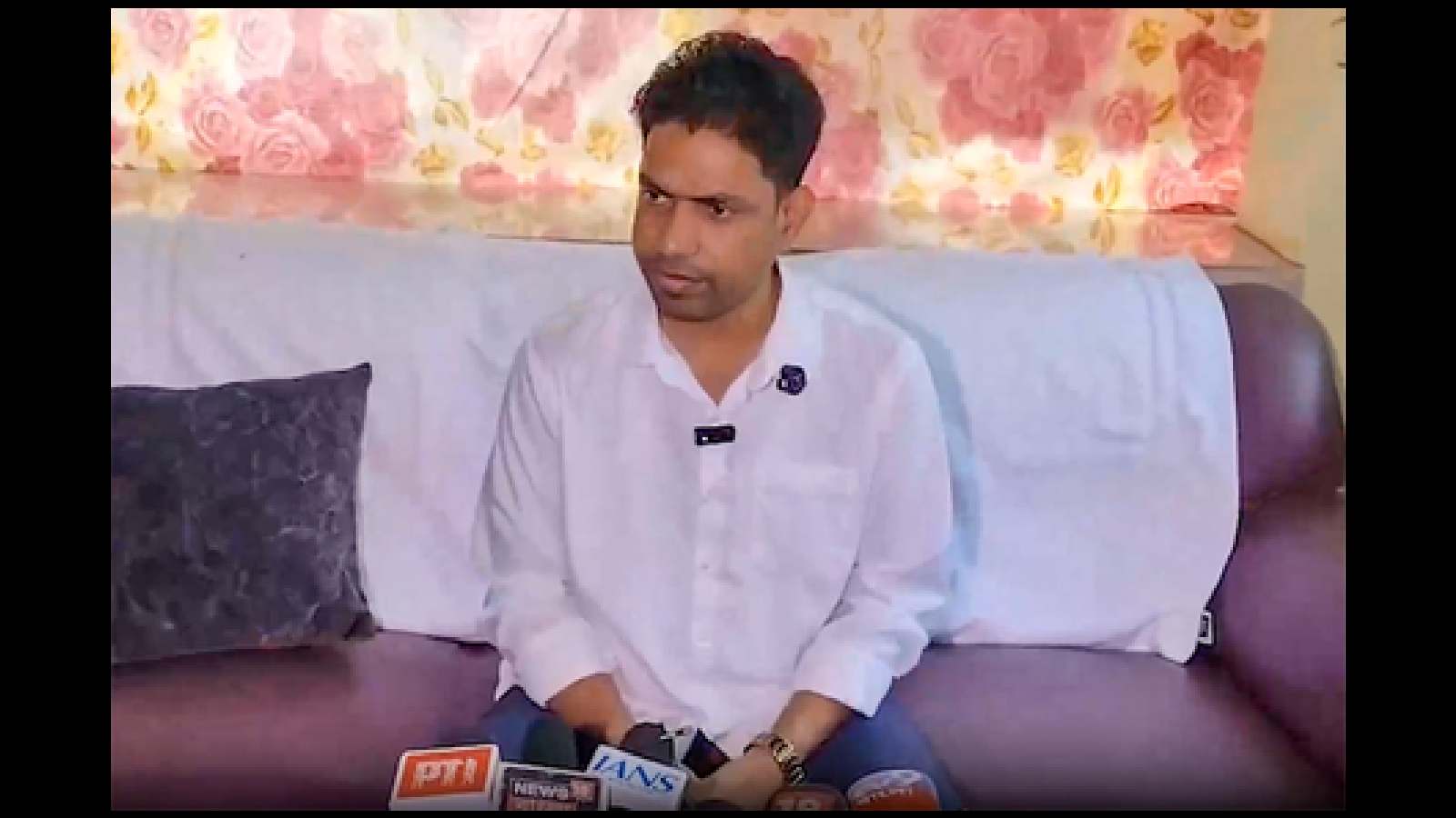 A young man in a white shirt sitting on a sofa during an interview at The Siasat Daily.