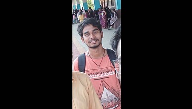 A young man smiling at a public event, wearing a red t-shirt and carrying a backpack.