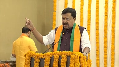 Nitin Nabin speaking passionately at a political event with yellow and orange decorations.