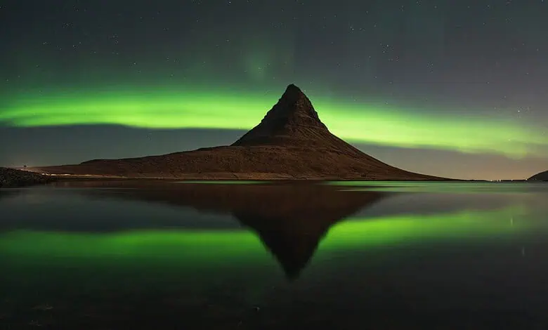Aurora Borealis over Kirkjufell mountain in Iceland at night, reflecting on calm water.