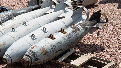 Explosive devices or missiles laid on the ground with rusted surfaces and metal fins.