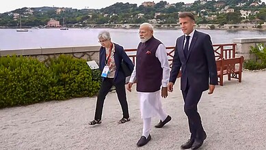 Indian Prime Minister Narendra Modi walking along a riverside with two officials, scenic background with.