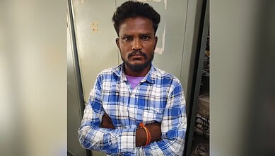 Young man with crossed arms wearing a blue checkered shirt in front of a grey background.