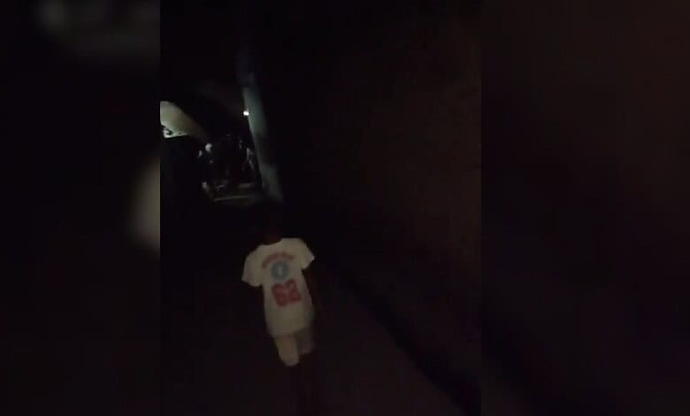 Child walking alone in a dark alley at night with a white T-shirt.