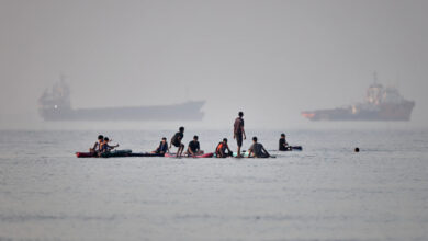 People gather on paddleboards in shallow water as cargo and service vessels are anchored in the Strait of Hormuz off Bandar Abbas in Iran