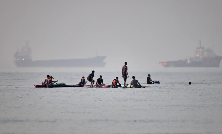 People gather on paddleboards in shallow water as cargo and service vessels are anchored in the Strait of Hormuz off Bandar Abbas in Iran