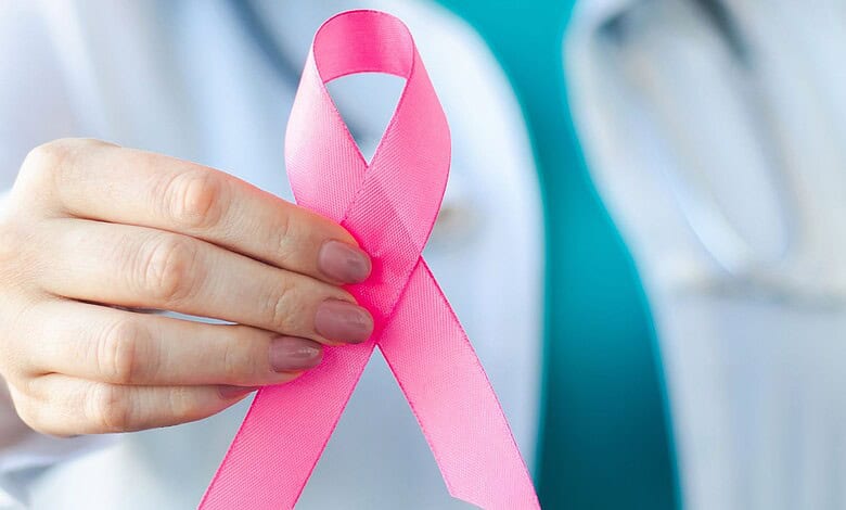 Pink ribbon for breast cancer awareness held by a healthcare professional.